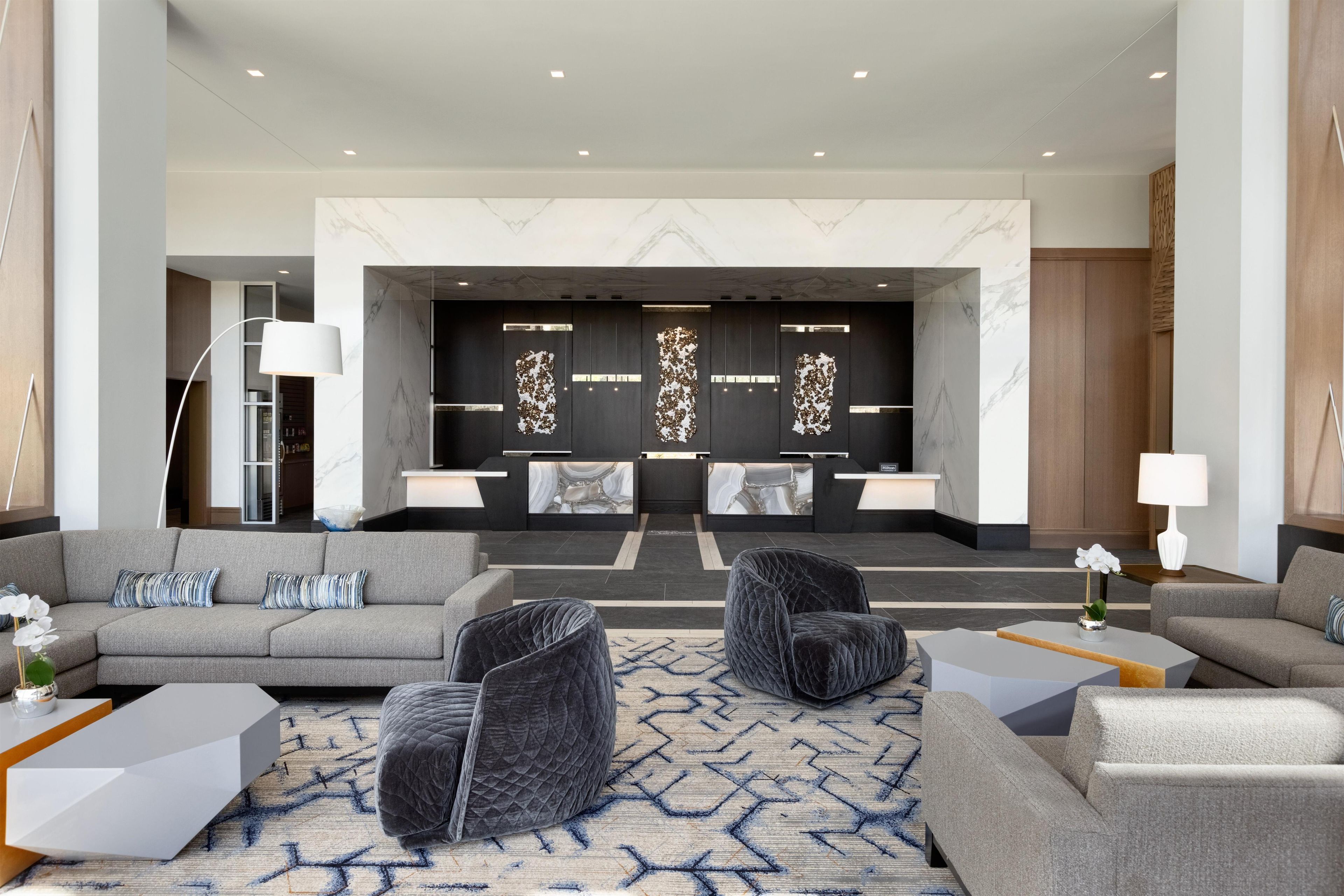 A modern lobby with a reception desk, seating area, and a decorative wall.
