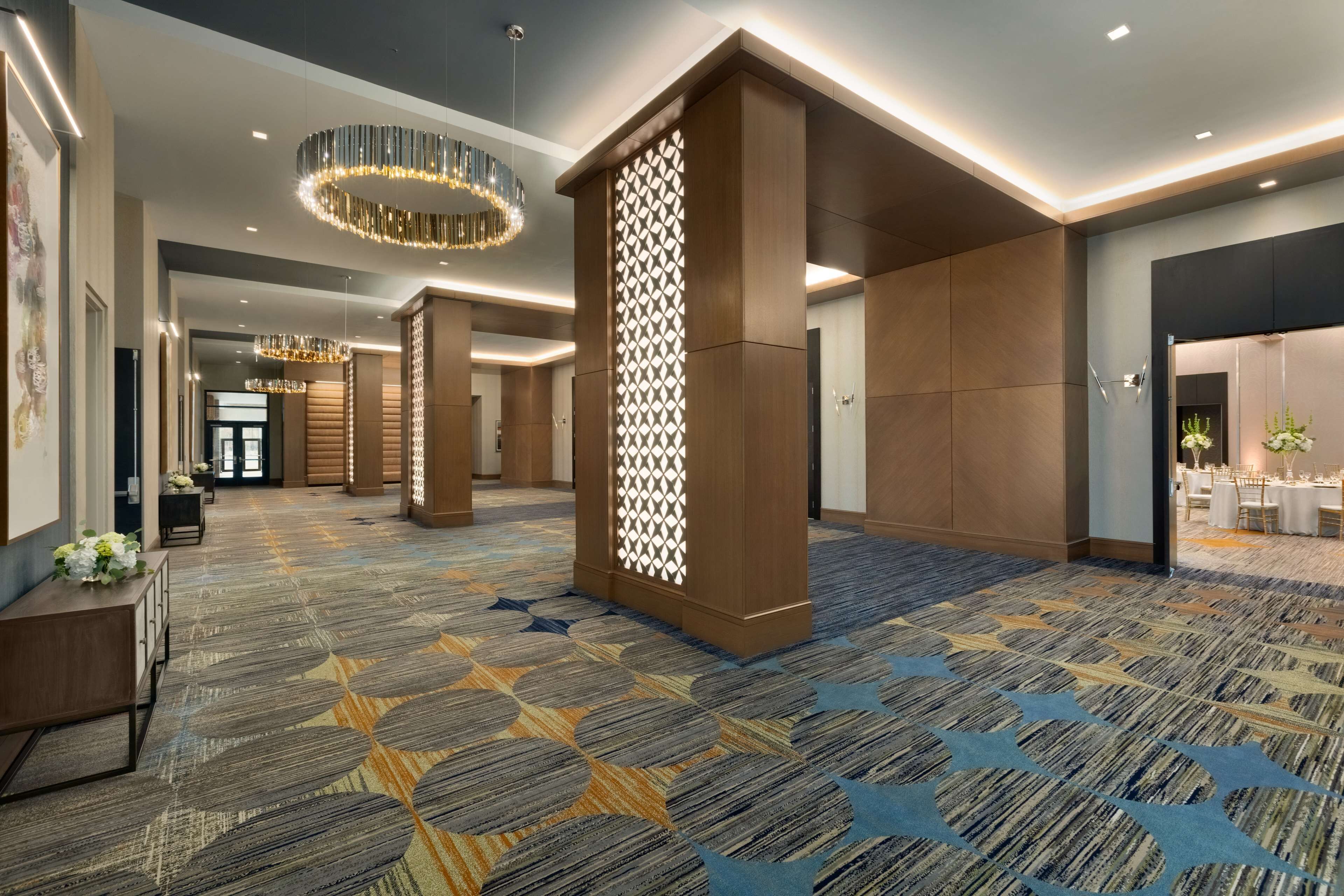 A spacious hotel lobby with a patterned carpet, modern lighting fixtures, and a reception area.
