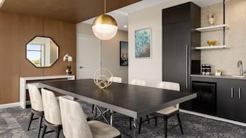 A modern dining area with a dark wooden table, six chairs, a pendant light, and a kitchen with dark cabinets and a tiled backsplash.