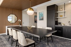 A modern dining area with a dark wooden table, six chairs, a pendant light, and a kitchen with dark cabinets and a tiled backsplash. - Hilton Alpharetta Atlanta (Alpharetta)