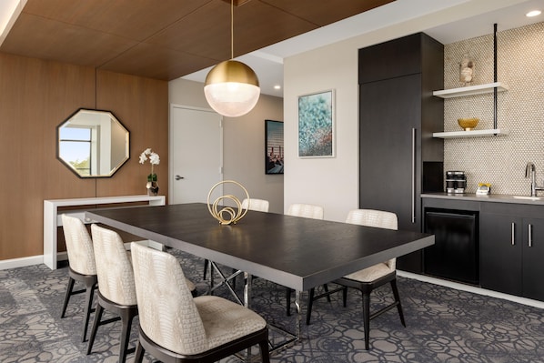 A modern dining area with a dark wooden table, six chairs, a pendant light, and a kitchen with dark cabinets and a tiled backsplash. - Hilton Alpharetta Atlanta (Alpharetta)