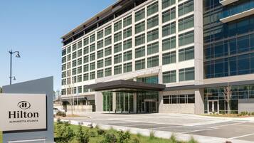 A modern hotel building with a large glass facade, a covered entrance, and a sign indicating it's the Hilton Alpharetta Atlanta.