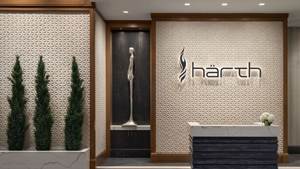 A reception area with a modern design, featuring a textured wall, a reception desk, and three potted plants. - Hilton Alpharetta Atlanta (Alpharetta)