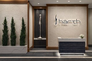 A reception area with a modern design, featuring a textured wall, a reception desk, and three potted plants. - Hilton Alpharetta Atlanta (Alpharetta)
