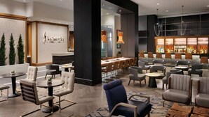 A modern hotel lobby with a bar area, seating arrangements, and a decorative wall with a logo. - Hilton Alpharetta Atlanta (Alpharetta)
