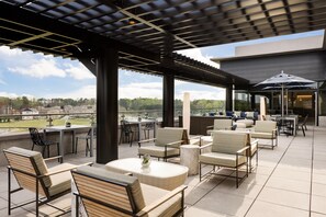 An outdoor patio area with seating arrangements, a pergola structure, and a view of the surrounding landscape. - Hilton Alpharetta Atlanta (Alpharetta)