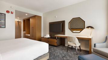A hotel room with a bed, a desk, a chair, a TV, and a mirror.