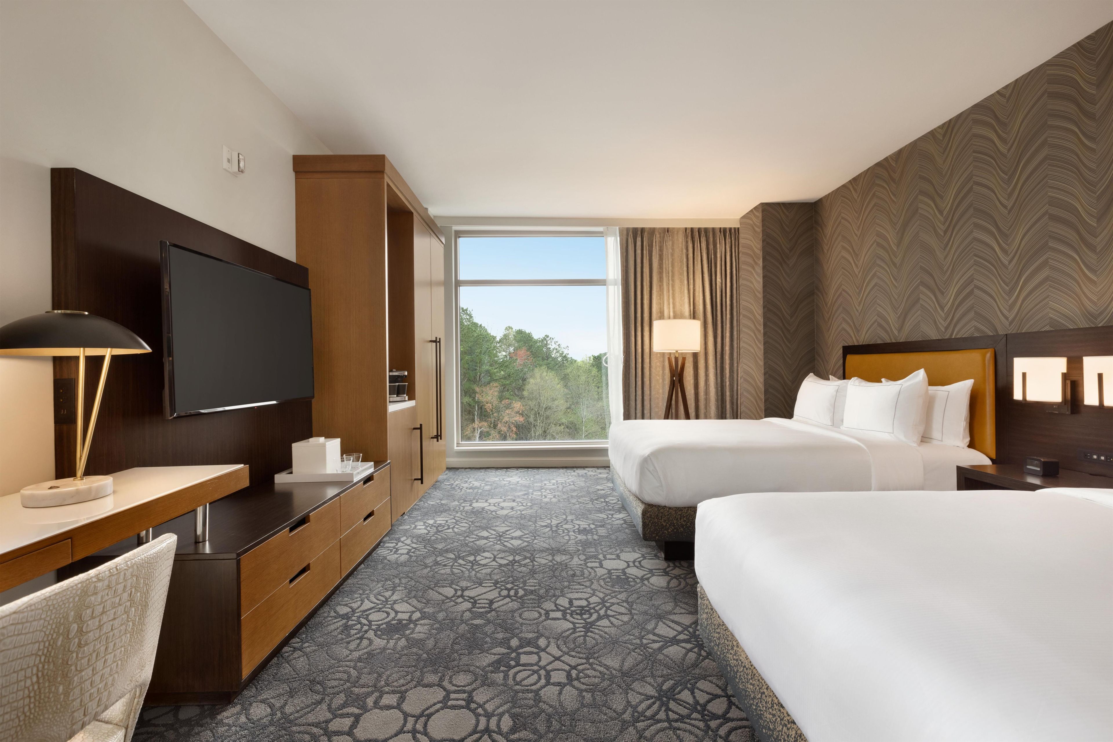 A hotel room with a large bed, a desk with a TV, a chair, and a window with curtains.