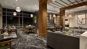 A modern dining area with round tables, cushioned seating, and pendant lighting. - Hilton Alpharetta Atlanta (Alpharetta)
