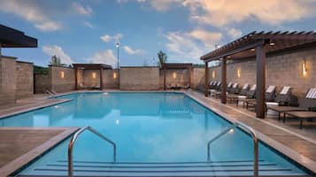 A rectangular swimming pool with a tiled deck, surrounded by lounge chairs and a pergola structure.