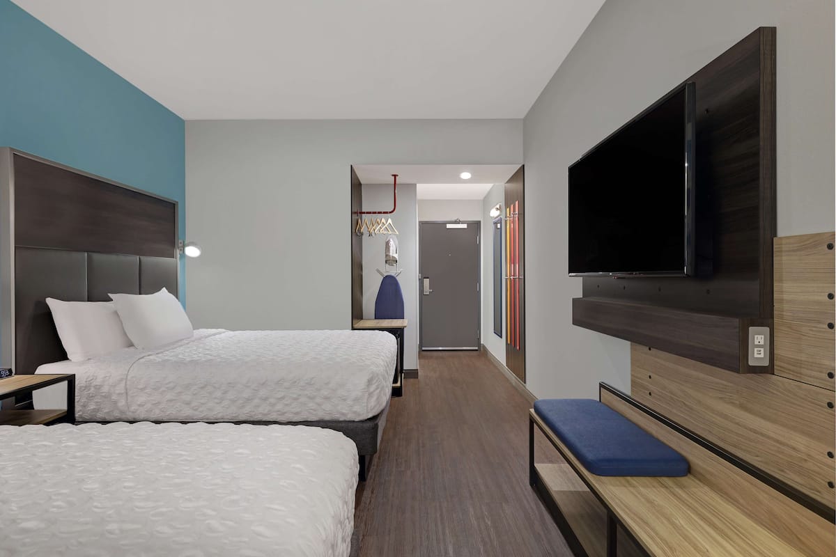 Ein Hotelzimmer mit zwei Betten, einem Fernseher, einer Bank und einem Kleiderschrank.