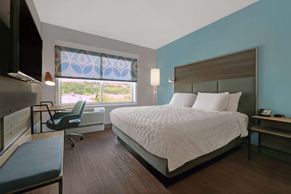 Ein Hotelzimmer mit Bett, Schreibtisch, Stuhl, Fenster mit Blick und einer Lampe.