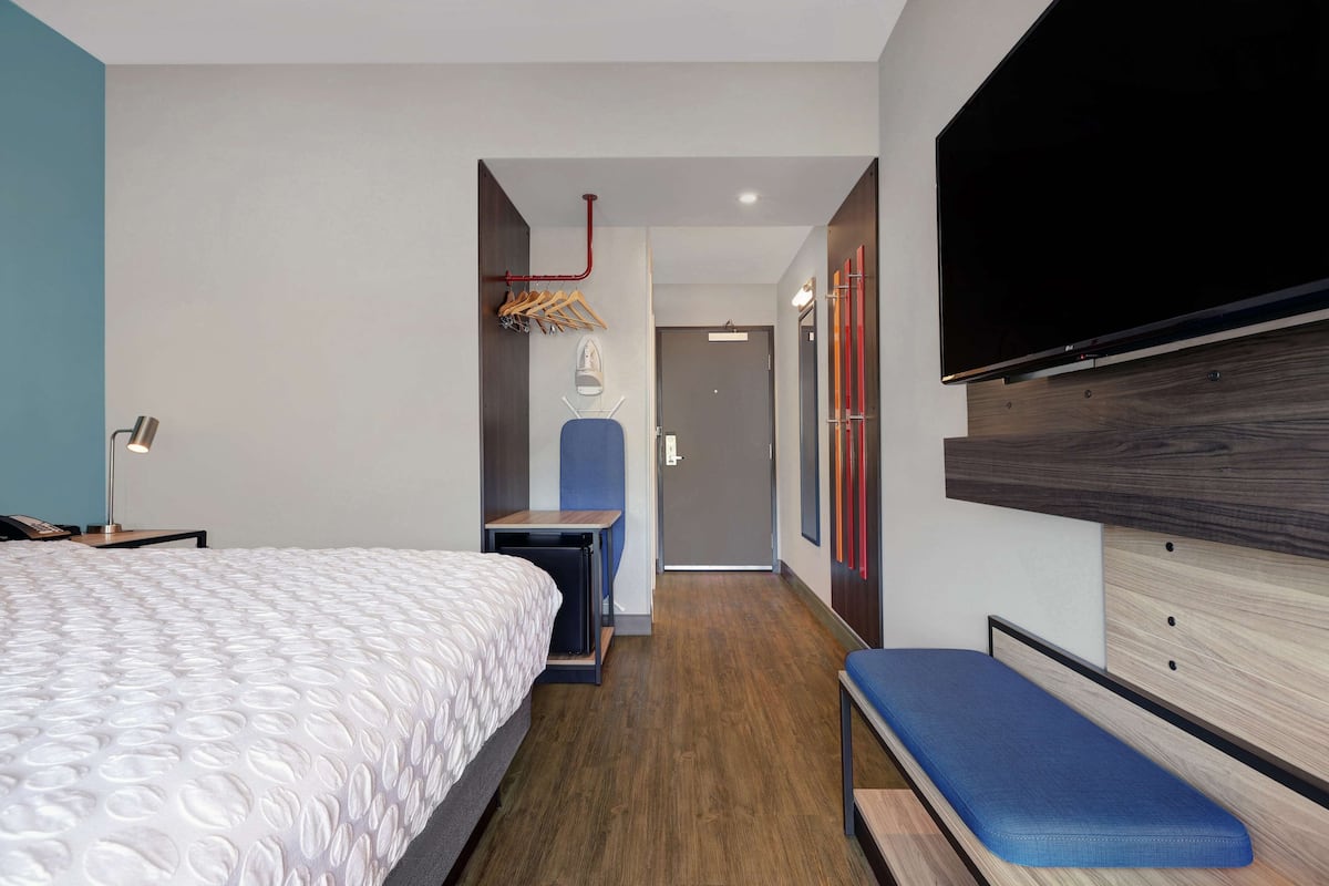 Ein modernes Hotelzimmer mit einem großen Bett, einem kleinen Schreibtisch, einer Bank, einem Fernseher und einem Kleiderschrank.