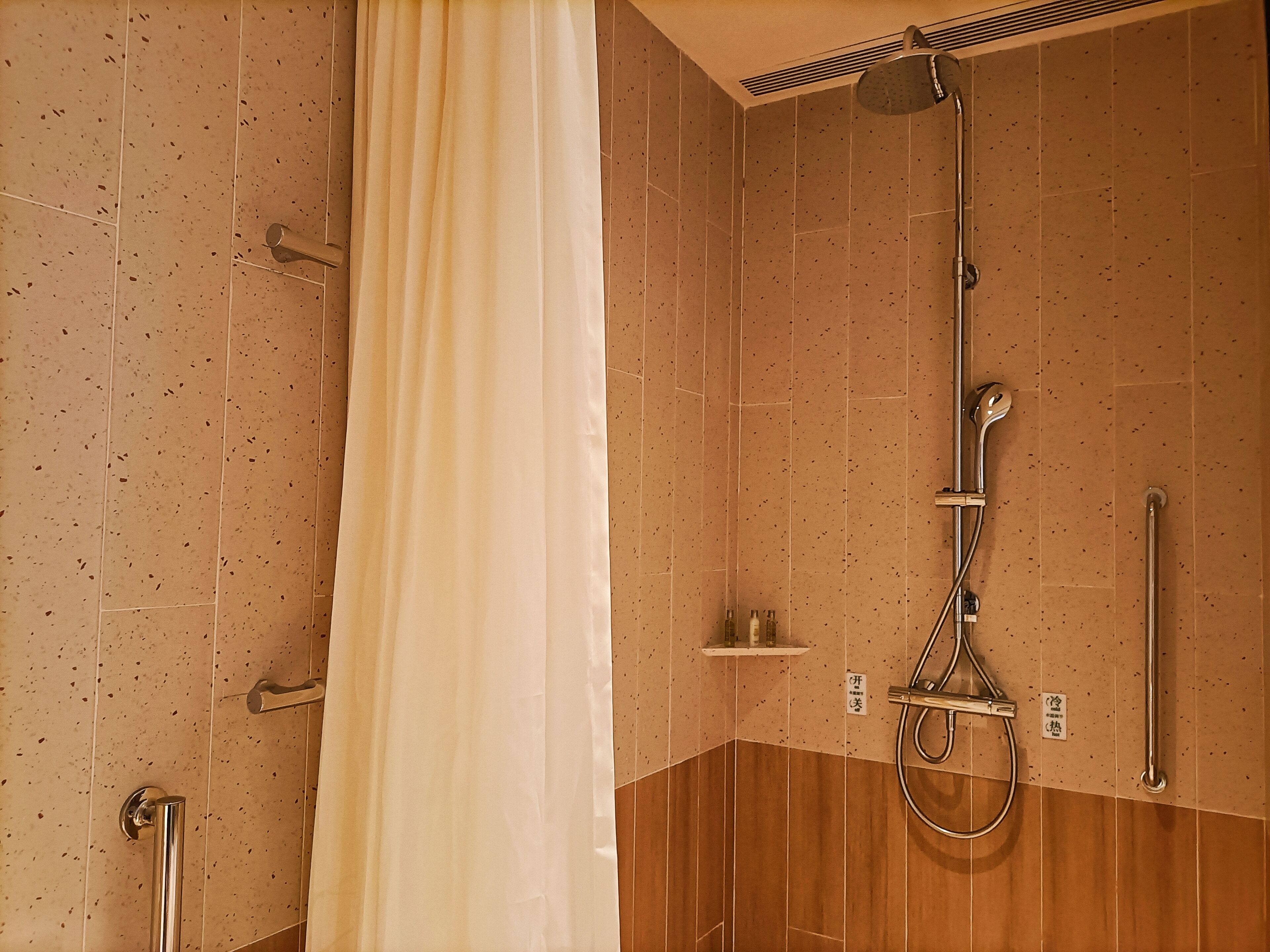 A shower area with a curtain, a handheld showerhead, a wall-mounted faucet, and a handheld showerhead.
