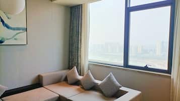 A modern living room with a sofa, pillows, a painting, and a large window with a city view.