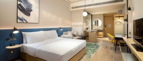 Habitación de hotel con una cama grande, mesita de noche con lámpara, escritorio con silla, espejo y televisión.