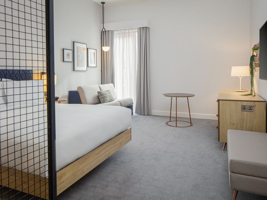 Una habitación de hotel con cama, sofá, una mesita, televisor y escritorio.