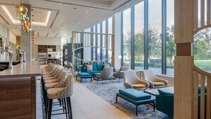 En modern hotellobby med en bardel, sittplatser och stora fönster som erbjuder utsikt över omgivningarna.