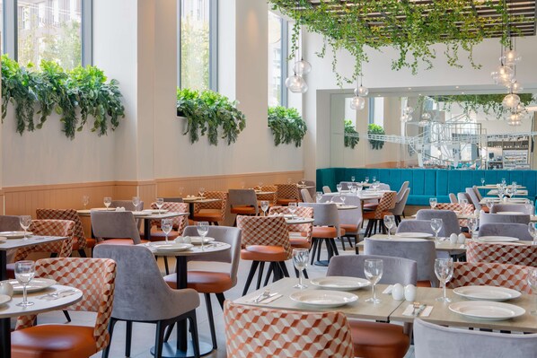 Un restaurante con mesas redondas, sillas a cuadros y plantas colgantes.