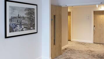 A hallway with a framed black and white historical building illustration, wooden doors, and patterned carpet flooring.