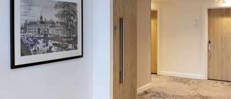A hallway with a framed black and white historical building illustration, wooden doors, and patterned carpet flooring.