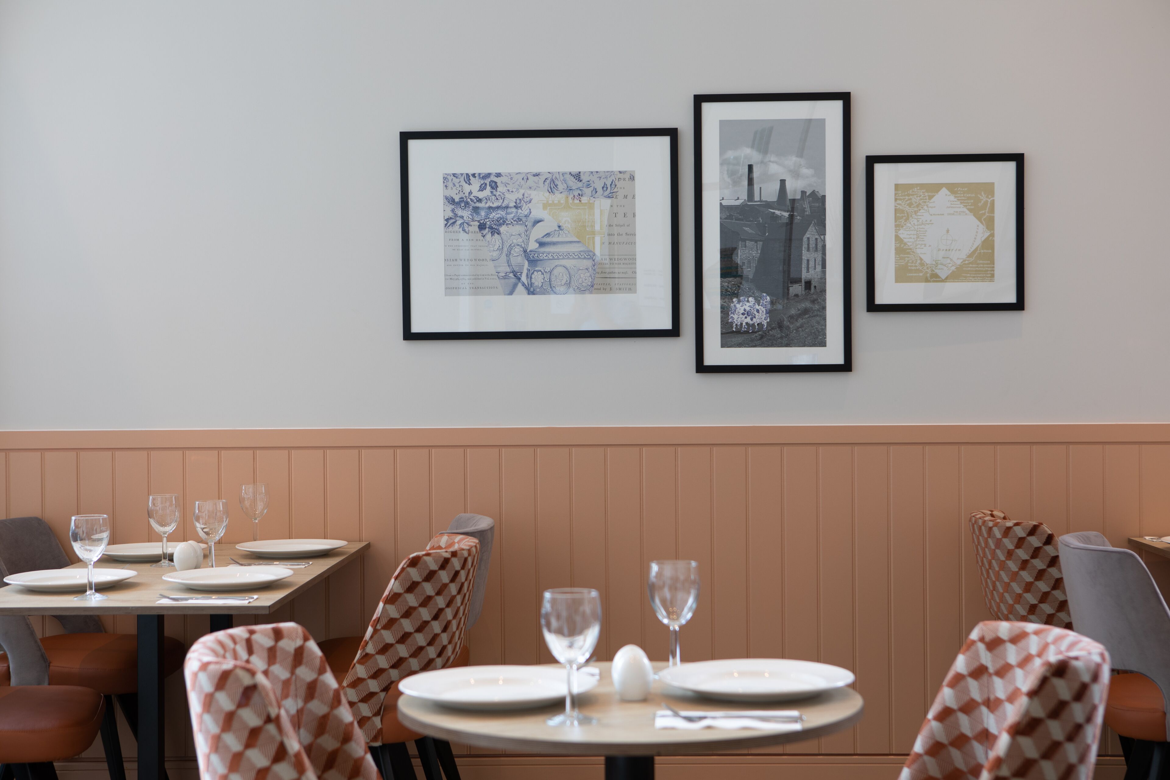 A restaurant interior with a dining area featuring checkered chairs, round tables, and framed artwork on the wall.