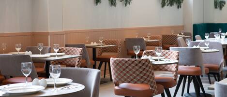 A restaurant with round tables and checkered chairs, featuring green plants on the walls and a teal booth area.