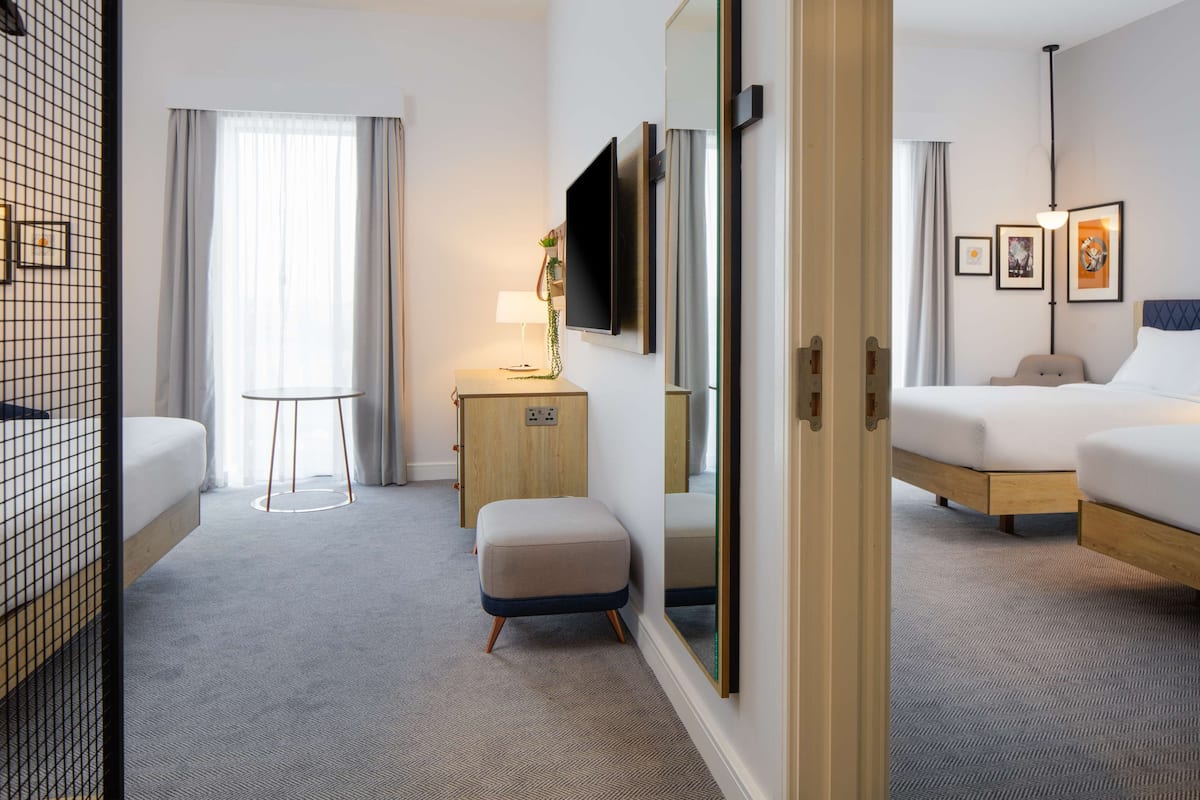 Een hotelkamer met een bed, een bureau, een stoel, een klein krukje, een televisie en een spiegel.
