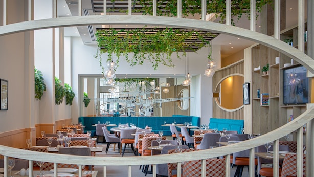 En modern restaurang med ett centralt placerat sittområde, flera matbord och ett urval av stolar.