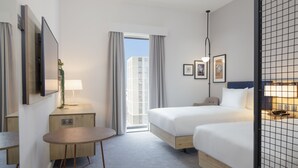 Ett hotellrum med två sängar, ett skrivbord, en stol, en lampa och utsikt över omgivningarna.