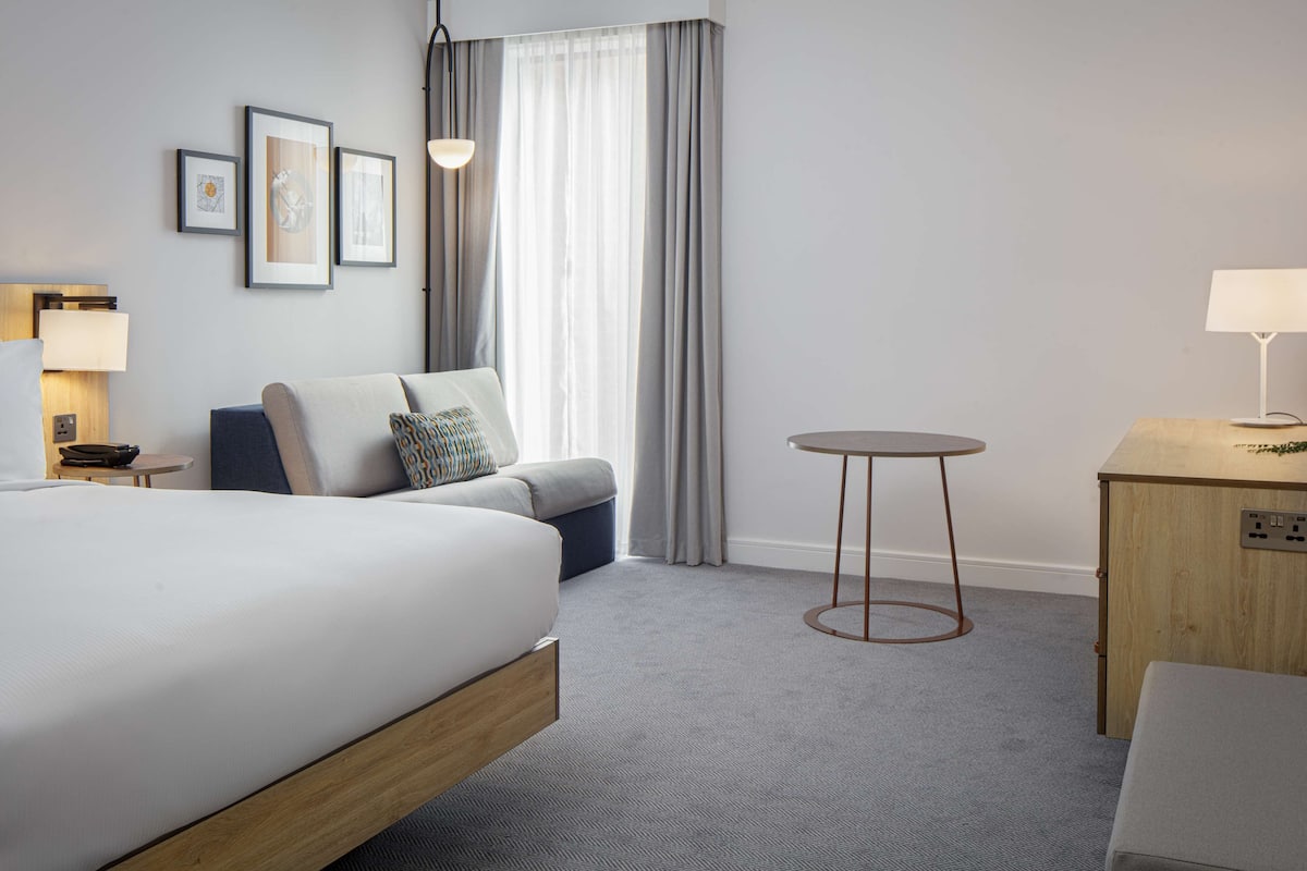 Een hotelkamer met een groot bed, een kleine zithoek, een ronde tafel en een bureau.