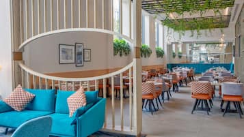A spacious indoor area with a curved white railing, teal sofas, and orange and white checkered chairs.