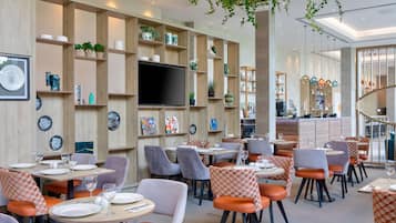 Um restaurante moderno com painéis de parede de madeira, uma televisão de tela plana e cadeiras estofadas em laranja e cinza.