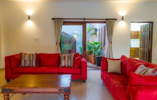 A living room with two red sofas, a wooden coffee table, and a sliding glass door leading to a patio with plants. - Vipingo Villa (Vipingo)