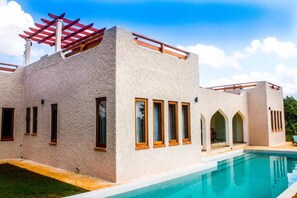 A modern building with a pool, featuring a unique architectural design with arched windows and a pergola.