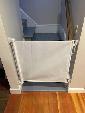 A room with a wooden floor, a white door with a white towel hanging on a white towel rack, and a staircase leading to another room.