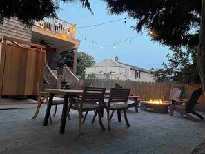 Een terras buiten met een eettafel, stoelen, een vuurkorf en sfeerverlichting.