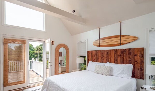 A bedroom with a large bed, a wooden headboard, a balcony door, and a wooden surfboard decoration.