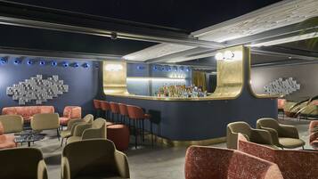 A bar area with a curved counter, seating with red and beige chairs, and a wall with a geometric light fixture.