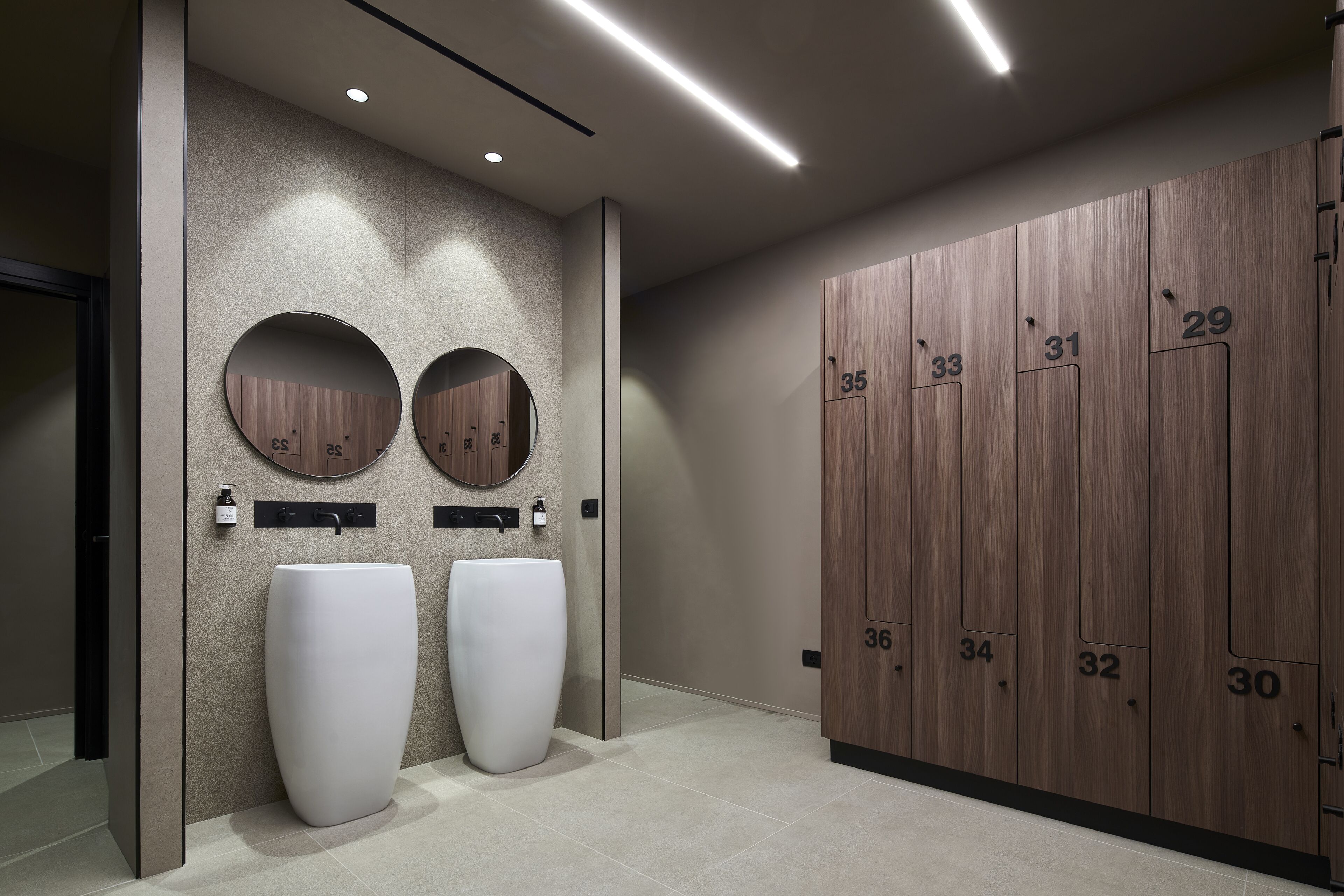 A modern restroom with two large sinks, a mirror, and a wooden locker wall with numbered compartments.