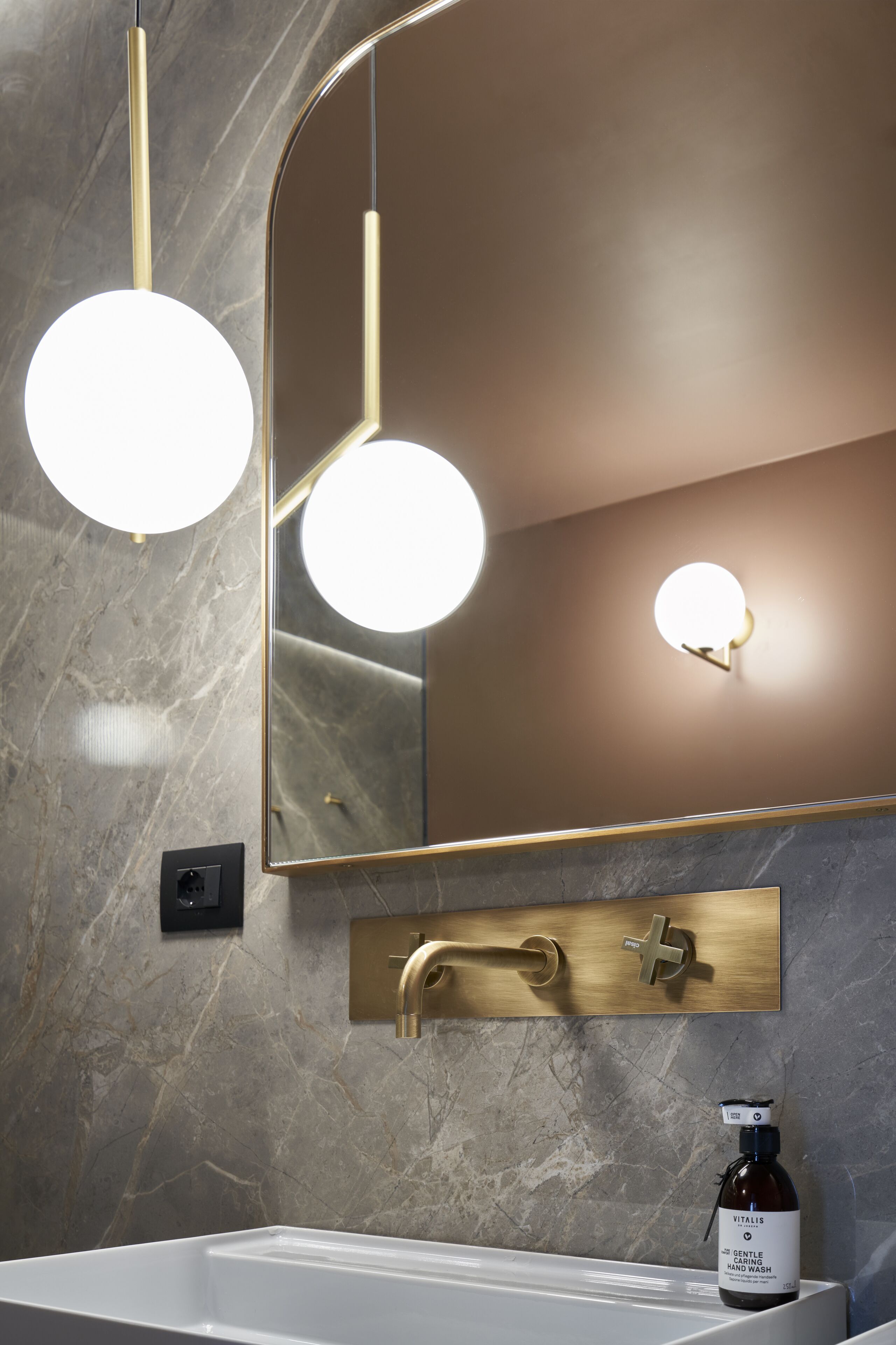 Een moderne badkamer met een witte wastafel, een gouden kraan en een grote spiegel met ingebouwde verlichting.