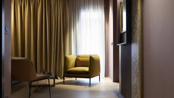 Una habitación moderna con sofá y sillón, un ventanal con cortinas y un televisor en la pared.