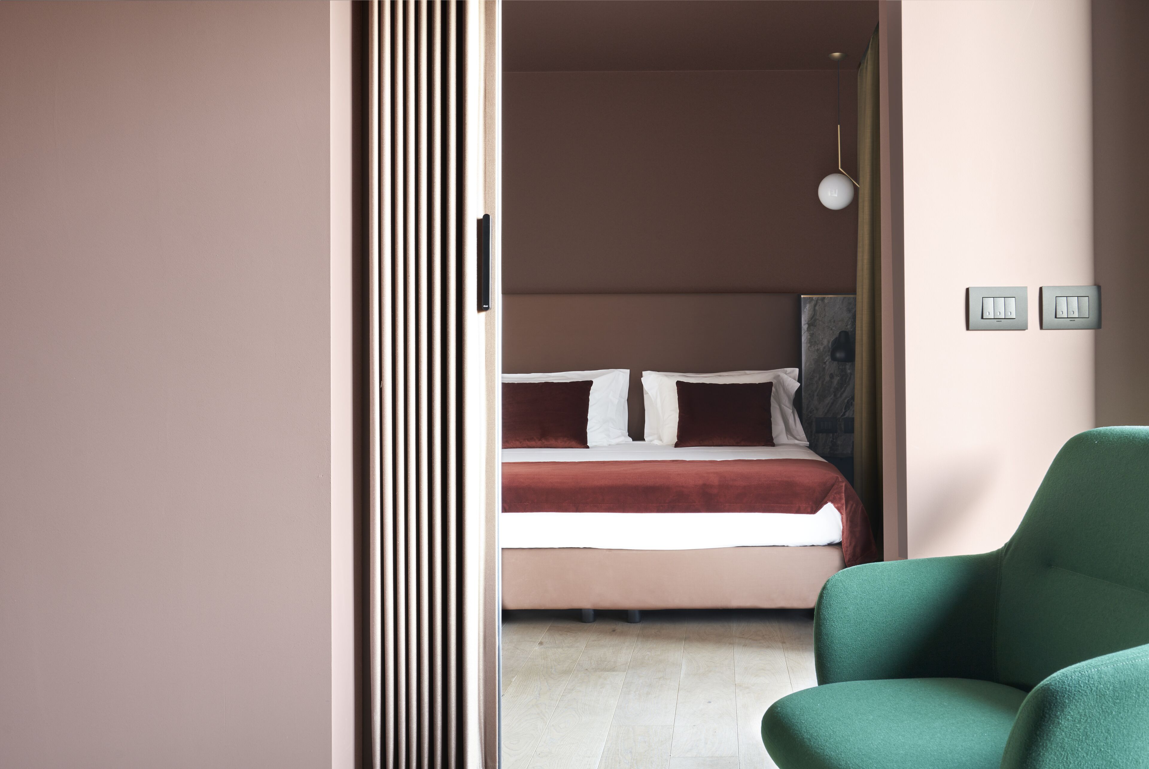 A bedroom with a bed, a green chair, and a wall-mounted light fixture.