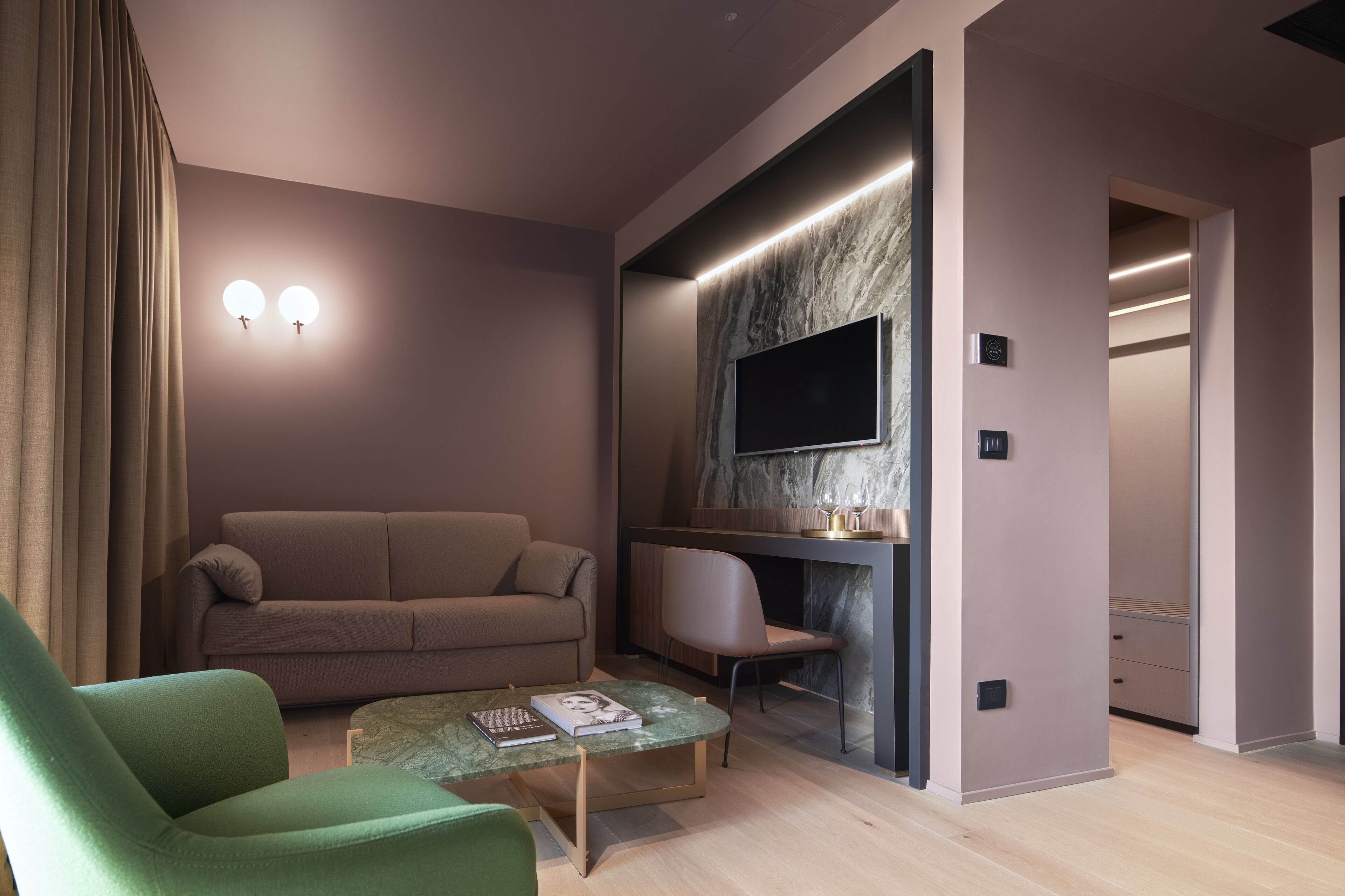 Ein modernes Wohnzimmer mit einer Couch, einem grünen Sessel, einem Marmortisch und einem flachbildfernseher, der an einer Marmorwand angebracht ist.
