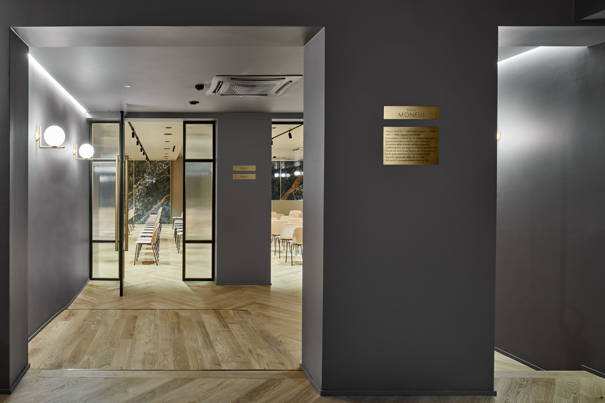 A modern interior with a wooden floor, glass doors leading to a seating area, and a plaque on the wall.