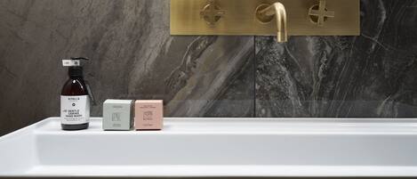 A bathroom with a marble wall, a gold faucet, and a bottle of hand wash soap.