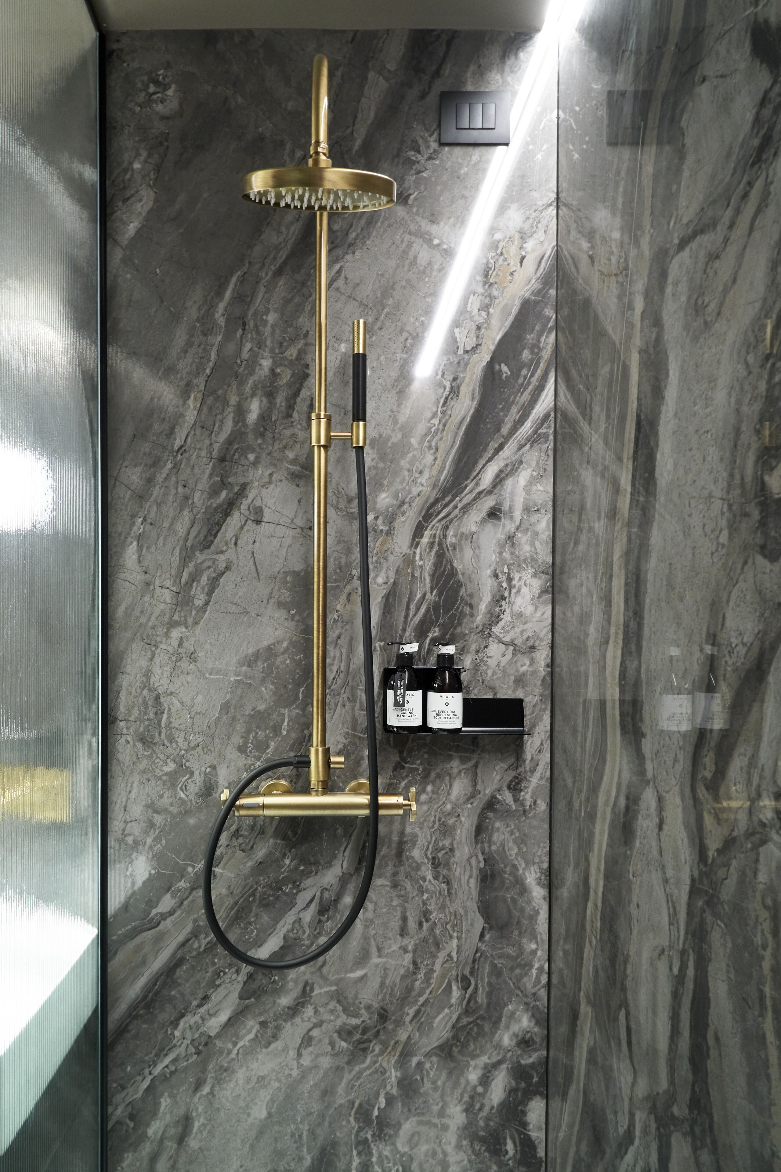 A modern shower with a gold finish, a handheld showerhead, and a handheld shower attachment.