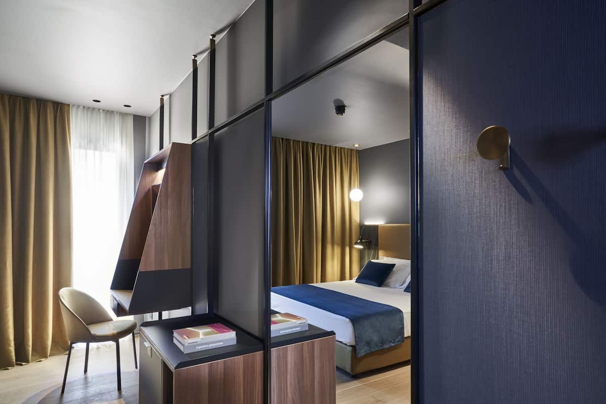 A modern hotel room with a desk, chair, and a bed with a blue blanket.