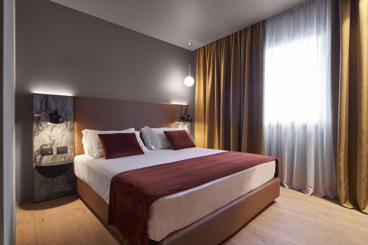A modern hotel room with a large bed, marble wall, and a bedside table with a lamp.