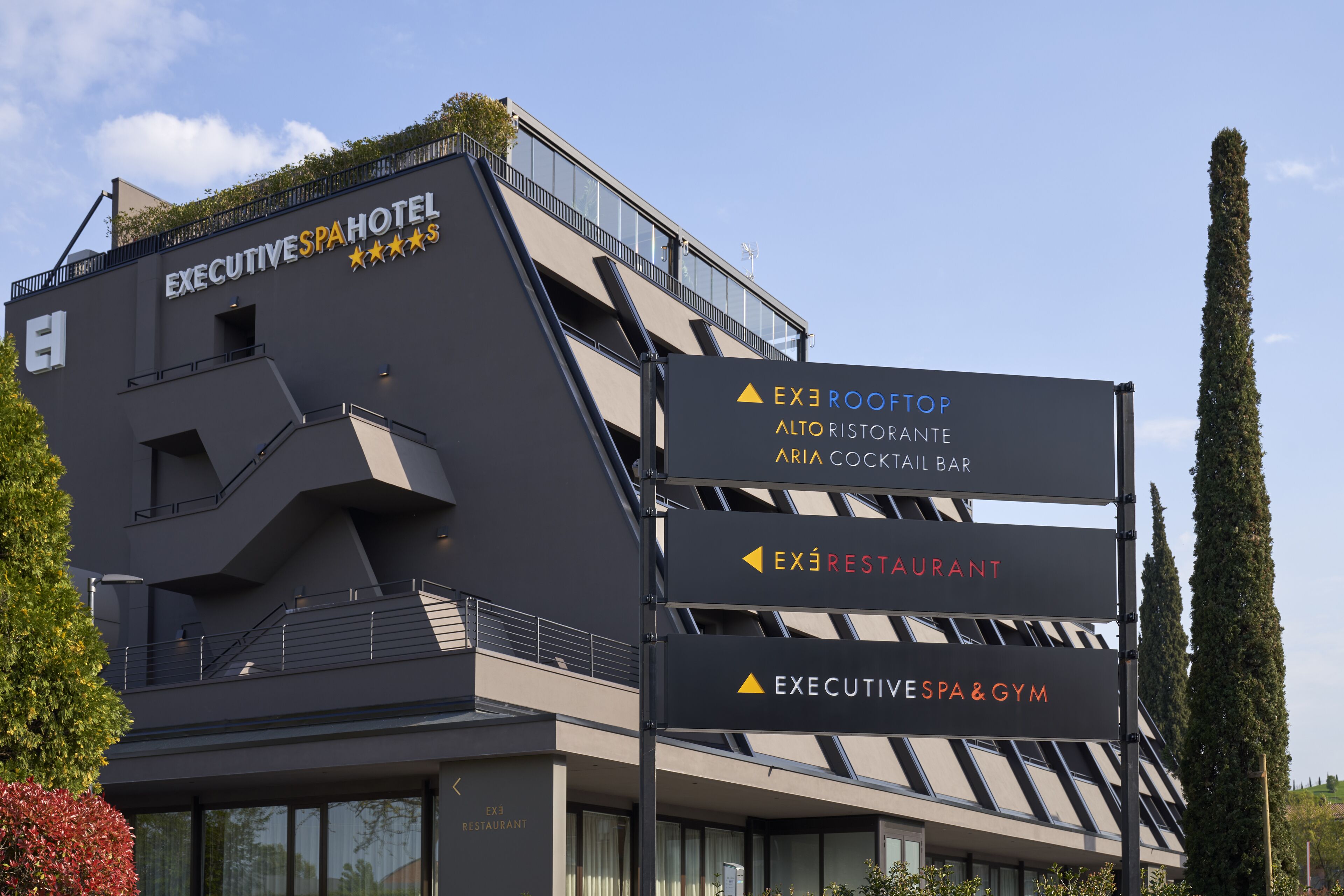 Um edifício moderno com a sinalização do Executive Spa Hotel, incluindo indicações para o Restaurante Executive, o Spa & Ginásio Executive e o Aria Cocktail Bar.